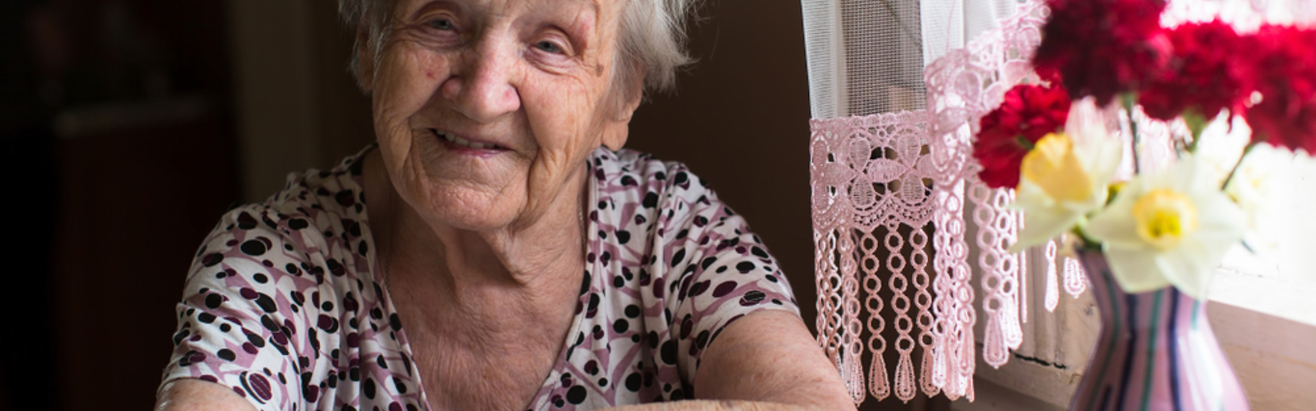 Older woman sitting at window smiling at camera